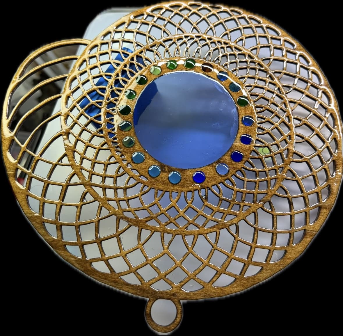 Intricate laser-cut wooden mandala with a central blue glass disc and colorful bead accents.